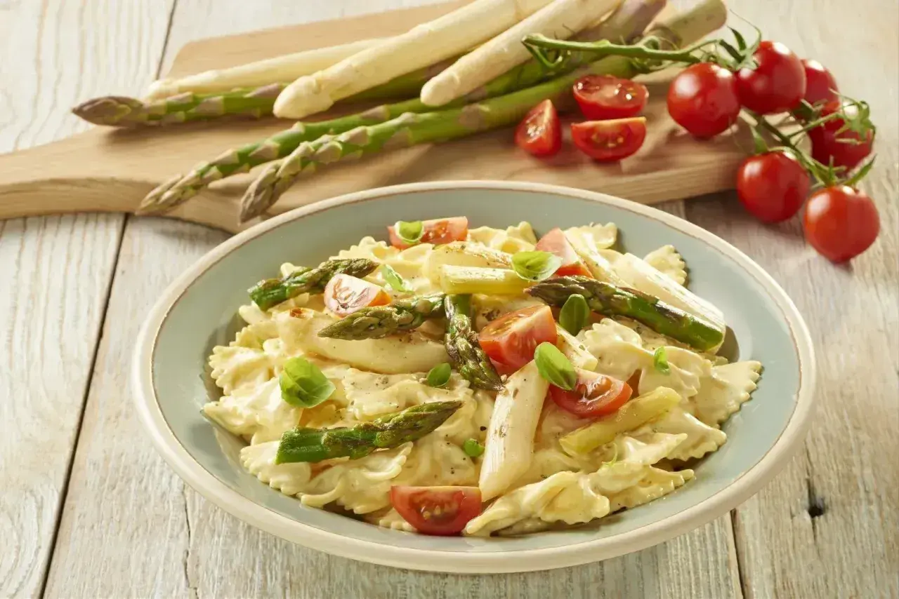 Pyszne szparagi na obiad w kremowym sosie z makaronem farfalle, pomidorkami i bazylią.