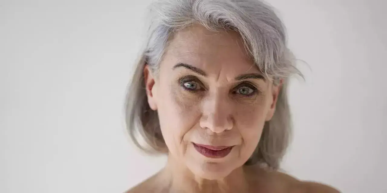 Primo piano di una donna con capelli grigi e pelle matura, che mostra i segni del tempo con grazia.