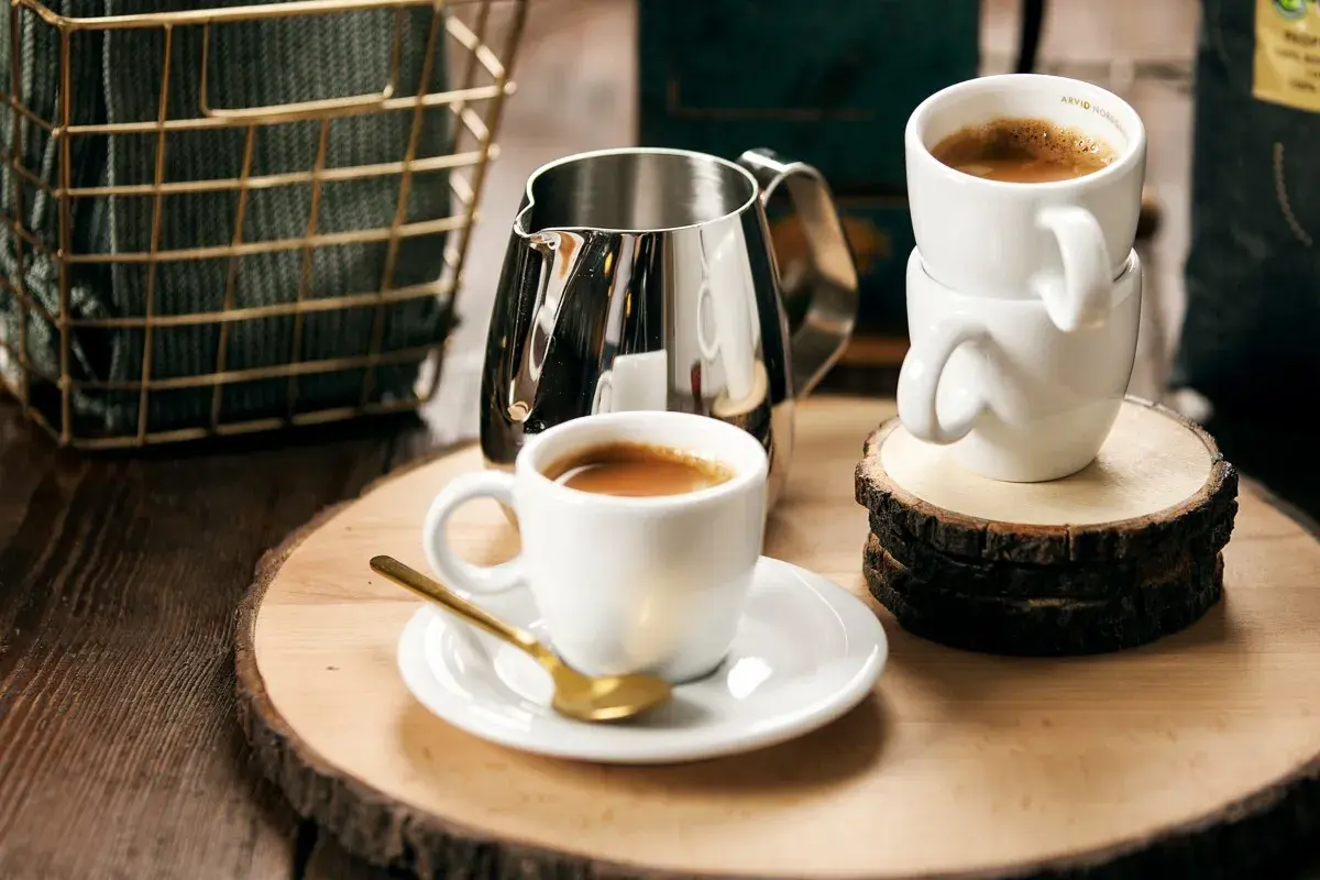Enkel espresso med gyllene sked och mjölkkanna. Två koppar står staplade på träbitar.
