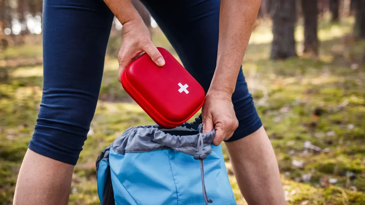 Person packt roten Erste Hilfe Set Inhalt in blauen Rucksack für Wanderung.