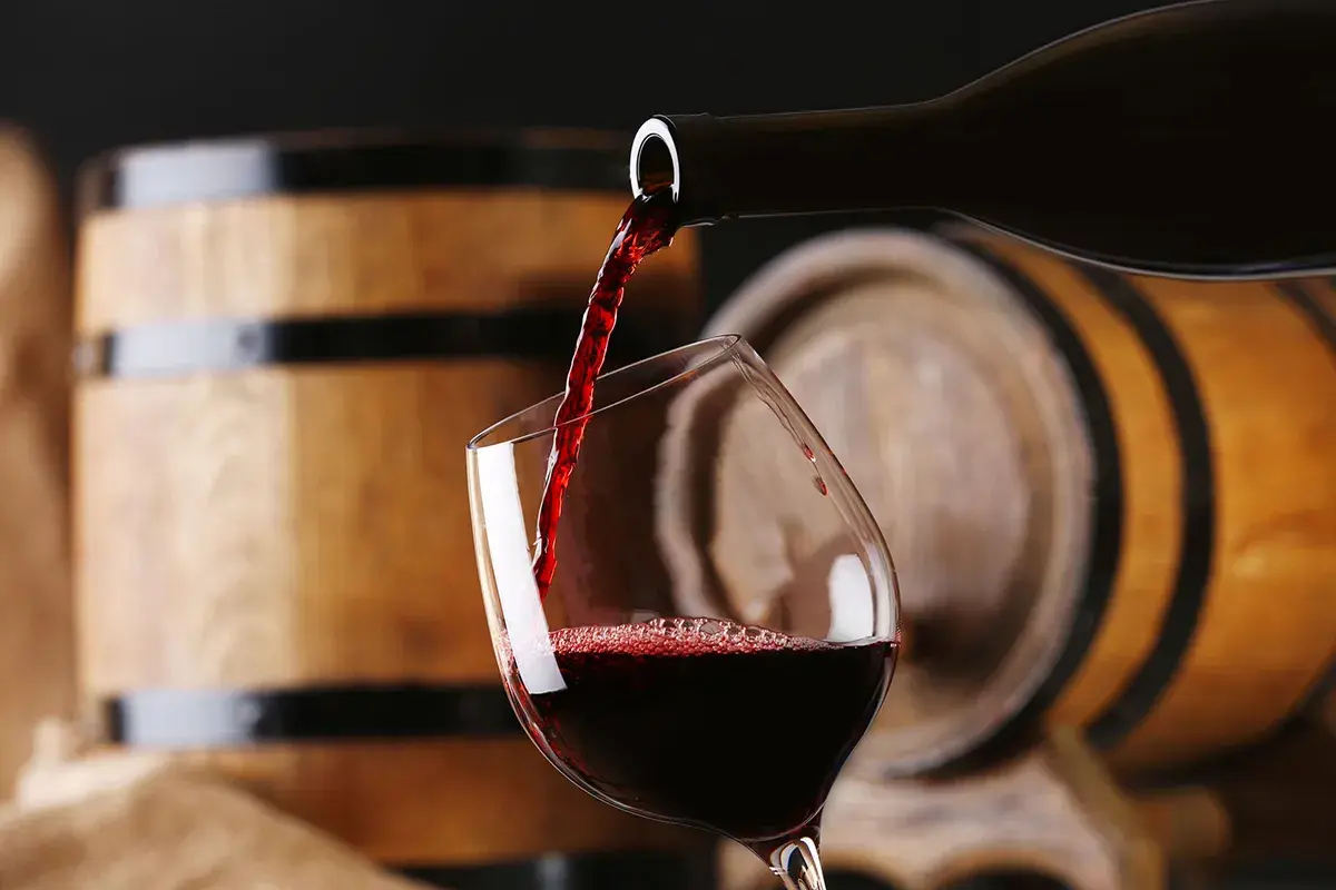 Versando un ricco aglianico vino in un bicchiere, con botti di legno sullo sfondo.