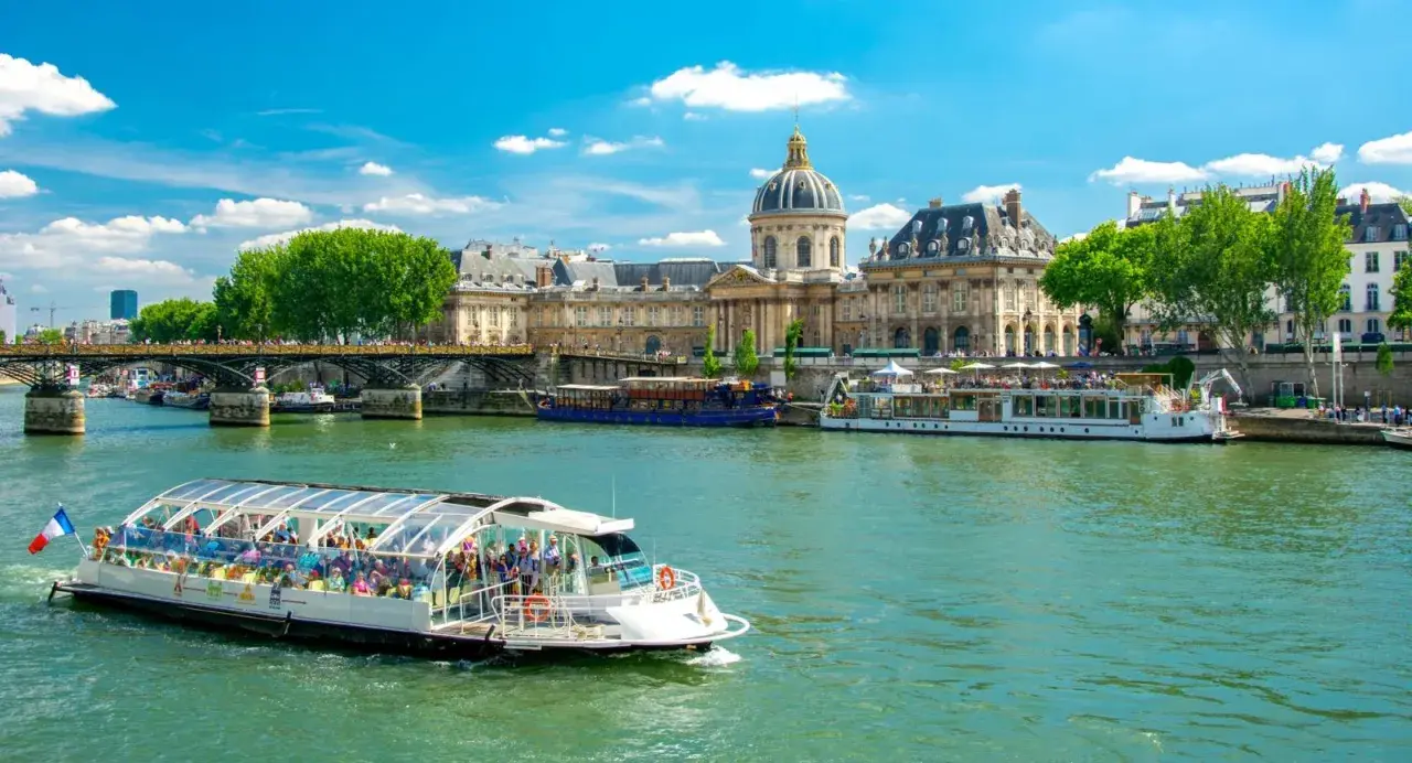 Bateau touristique sur la Seine, avec l'Institut de France et un pont en arrière-plan. Une belle journée pour une visite Paris Seine.