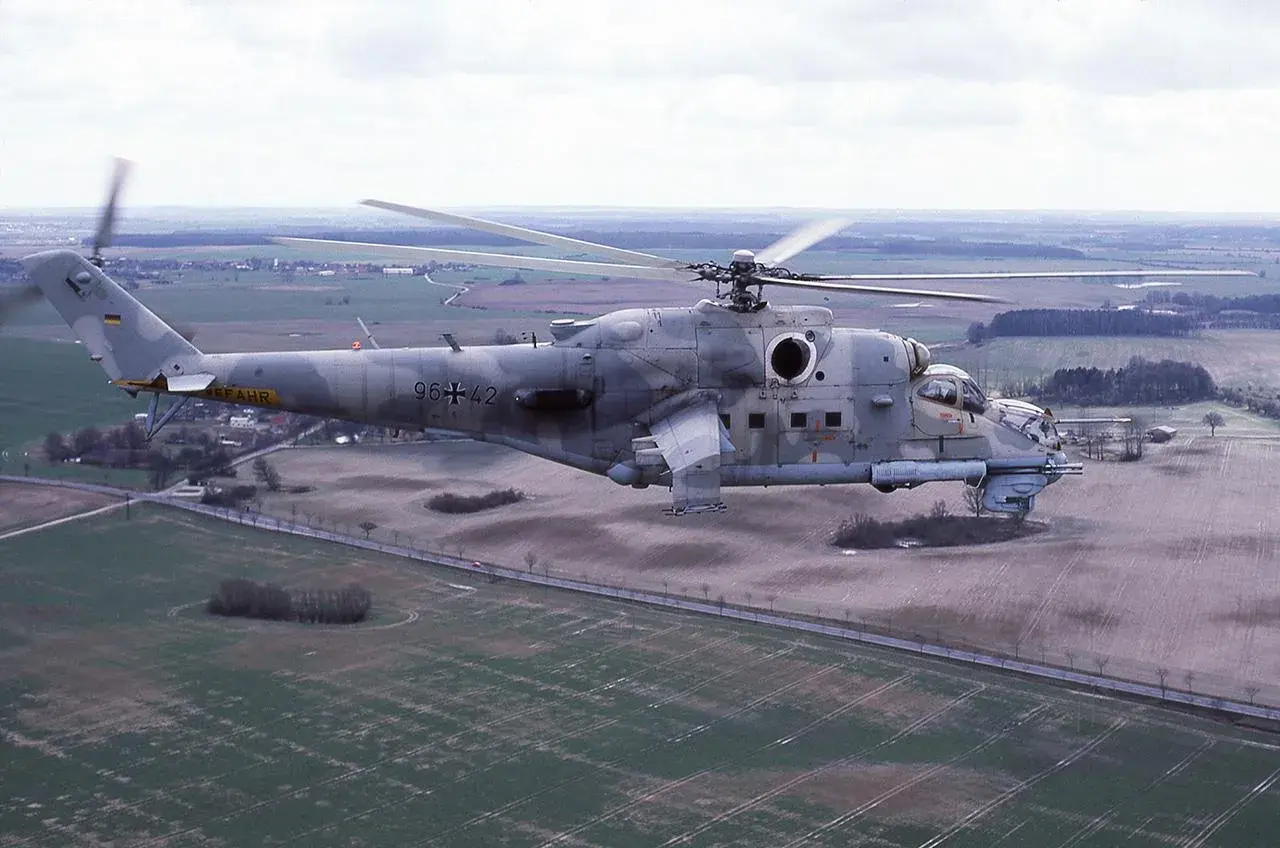 Ein Mi-24 Hind Hubschrauber der Bundeswehr fliegt über ein ländliches Gebiet.