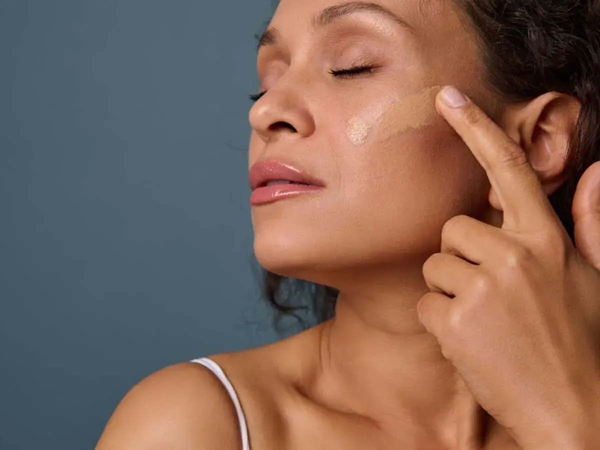 Application d'un fond de teint pour un maquillage teint parfait. Une femme applique délicatement le produit sur sa joue.
