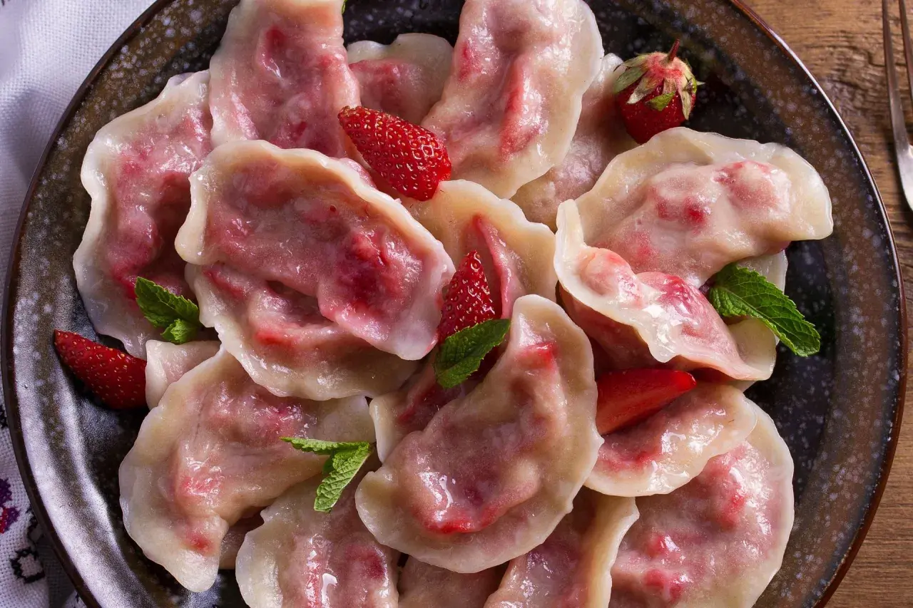 Pyszne pierogi z truskawkami, ozdobione świeżymi owocami i miętą, prezentują się apetycznie na talerzu.