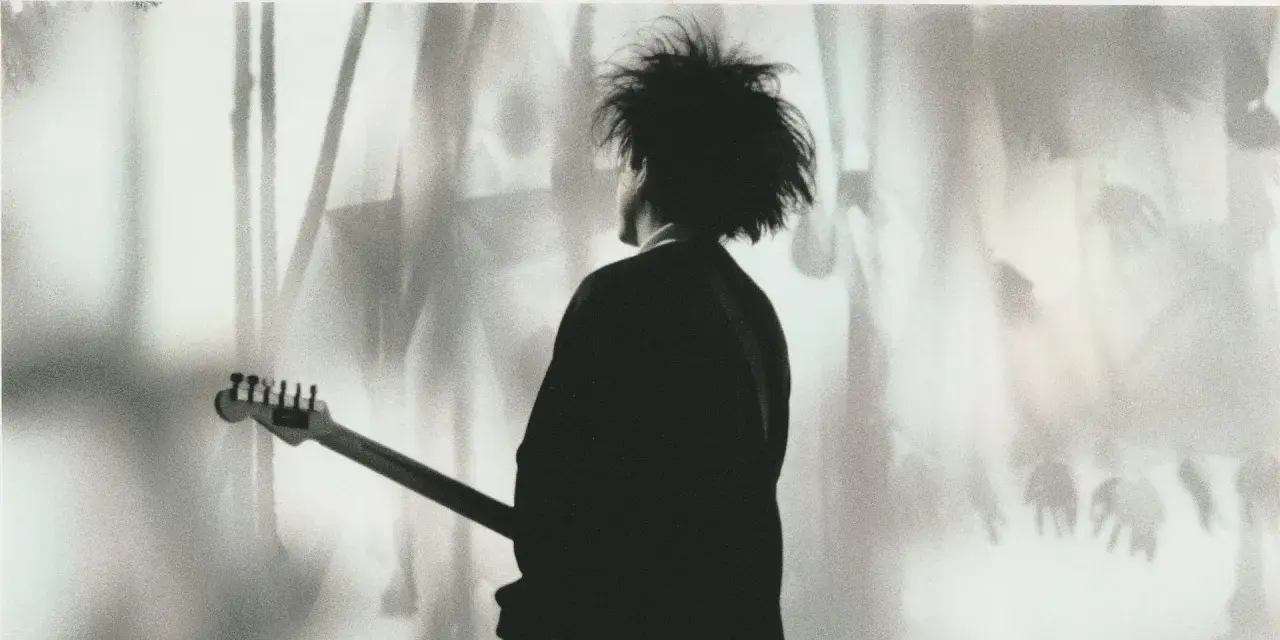 Chłopcy nie płaczą. Robert Smith z The Cure z gitarą, w cieniu, z charakterystyczną fryzurą.