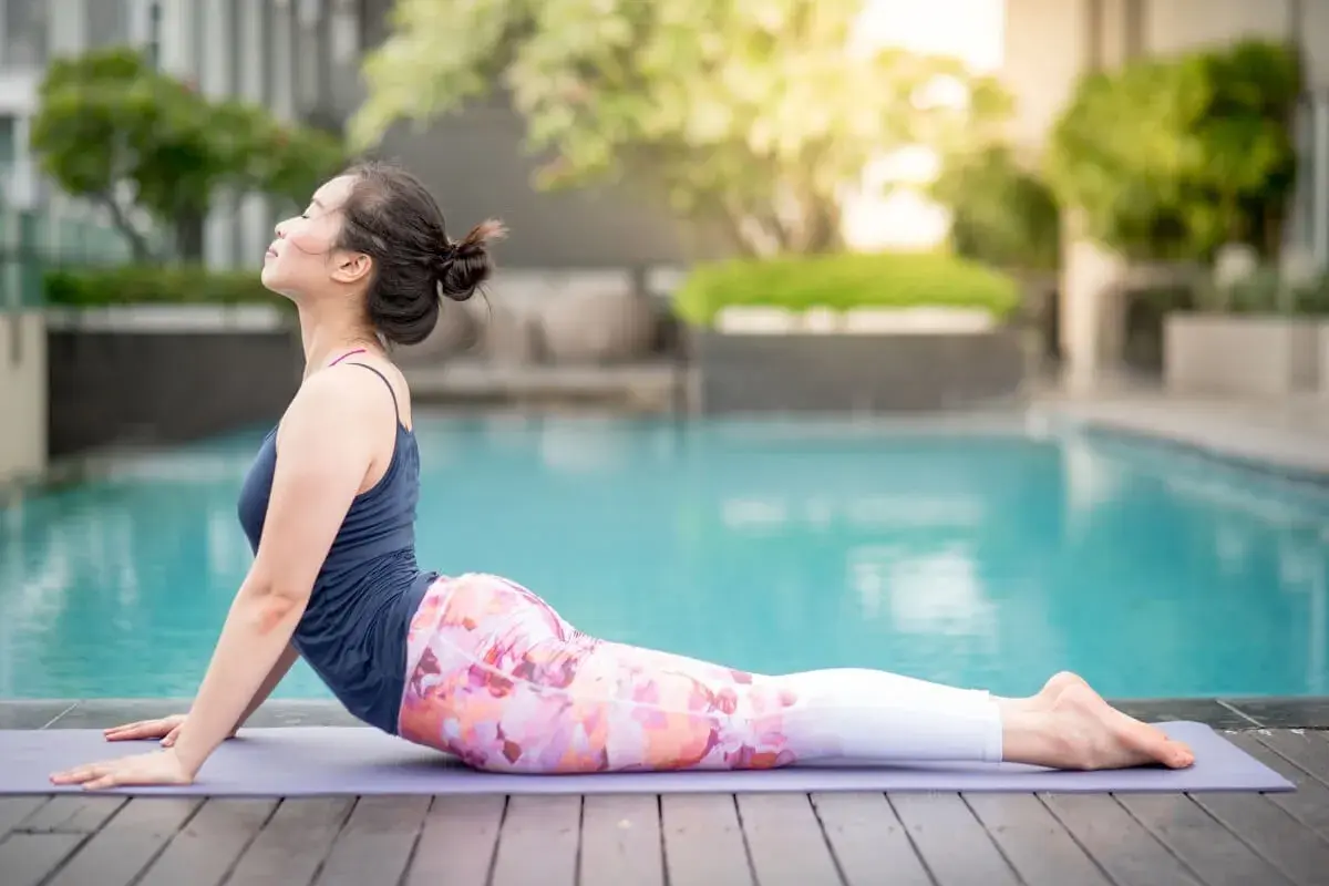 Kobieta w pozycji bhujangasana na macie przy basenie, zrelaksowana, z głową uniesioną do góry.