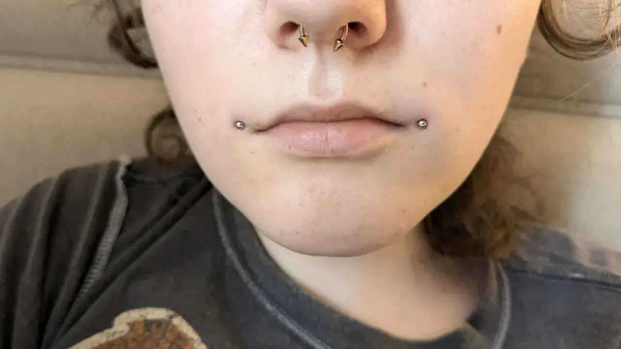 Dwa kolczyki dahlia piercing zdobią usta, dodając odważnego charakteru.
