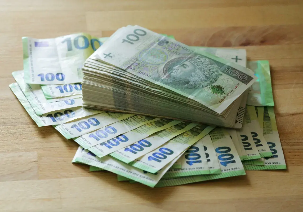 Stos banknotów 100 zł i 100 euro na drewnianym blacie. Może to być kwota na zasiłek stały.