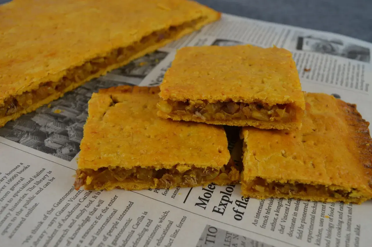 Coca amb tonyina, un delicioso pastel salado relleno de atún y cebolla, servido sobre un periódico.