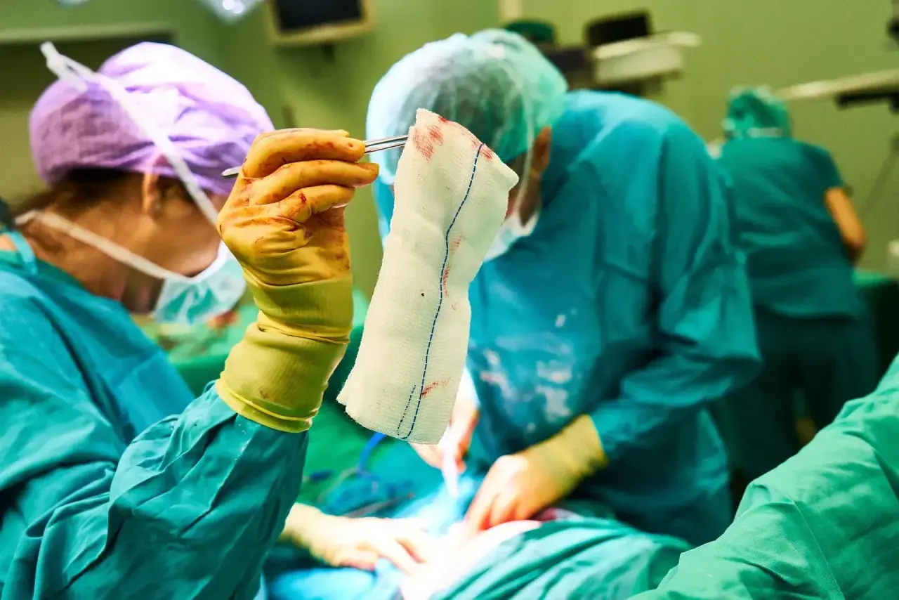 Chirurghi in sala operatoria. La mano guantata tiene una garza insanguinata, un dettaglio che potrebbe far pensare alle tabelle risarcimento malasanità morte.