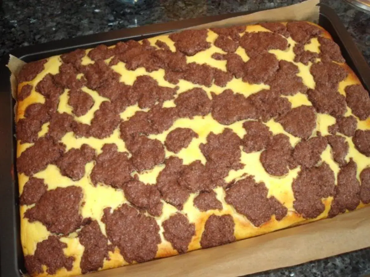 Ein frisch gebackener russischer Zupfkuchen im Blech, mit einem gelben Teig und dunklen Schokoladenstückchen darauf.