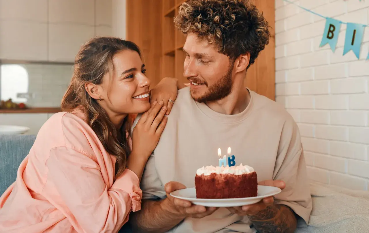 Pareja sonriente celebra un cumpleaños con un pastel. Ideas de frases bonitas para felicitar cumpleaños a tu pareja.