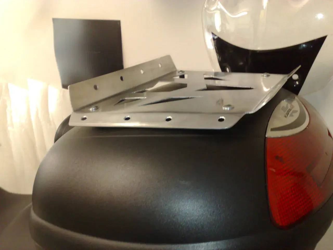 Piatto metallico forato, parte di un portapacchi moto fai da te, fissato su un bauletto nero.