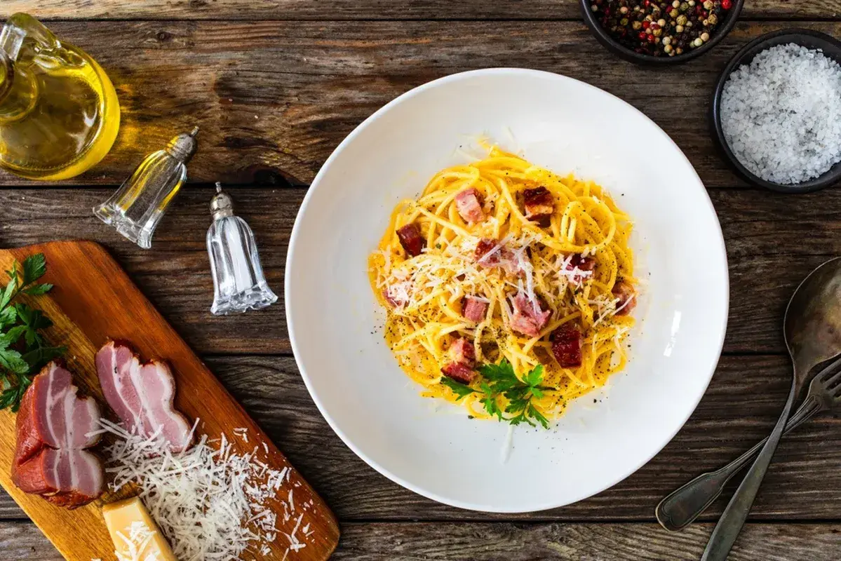 En tallrik krämig spaghetti carbonara med pancetta, toppad med parmesan och persilja. Perfekt vin till carbonara.