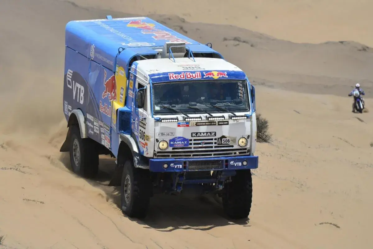 Camion Kamaz aux couleurs Red Bull, prêt à affronter le désert. La puissance camion Dakar se révèle dans ce paysage sablonneux.