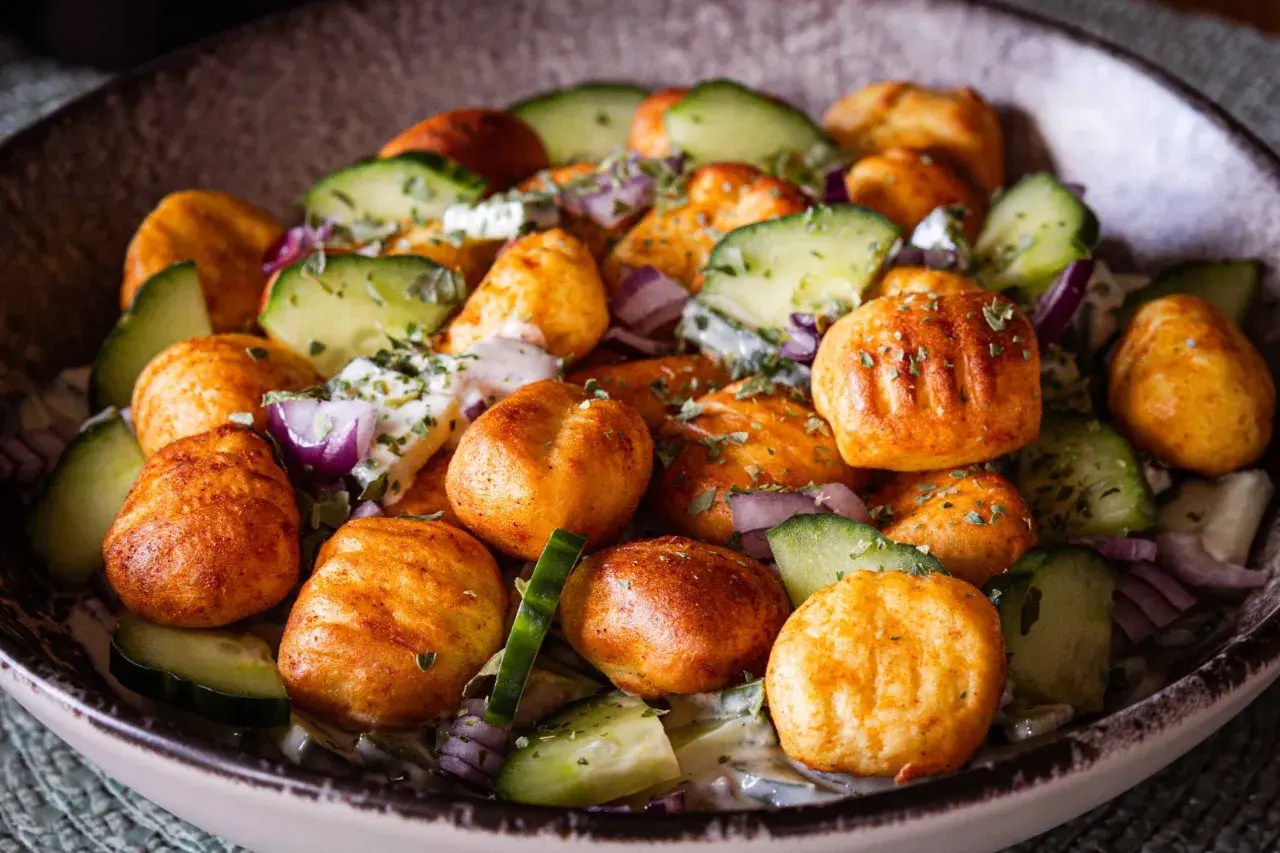 Knuspriger Gnocchi Salat mit Gurken, roten Zwiebeln und einem cremigen Dressing, garniert mit Kräutern.