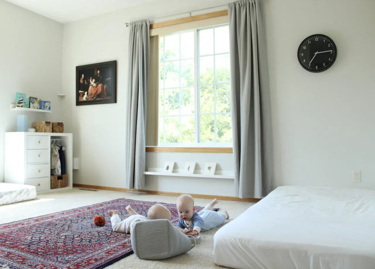 Two babies explore a room with a Montessori inspired feel, featuring a rug, toy basket, and artwork.