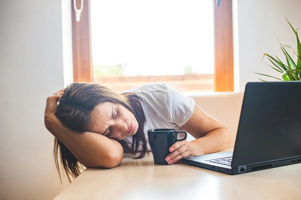 Donna esausta con tazza e laptop, forse cerca rimedi della nonna per la carenza di ferro.