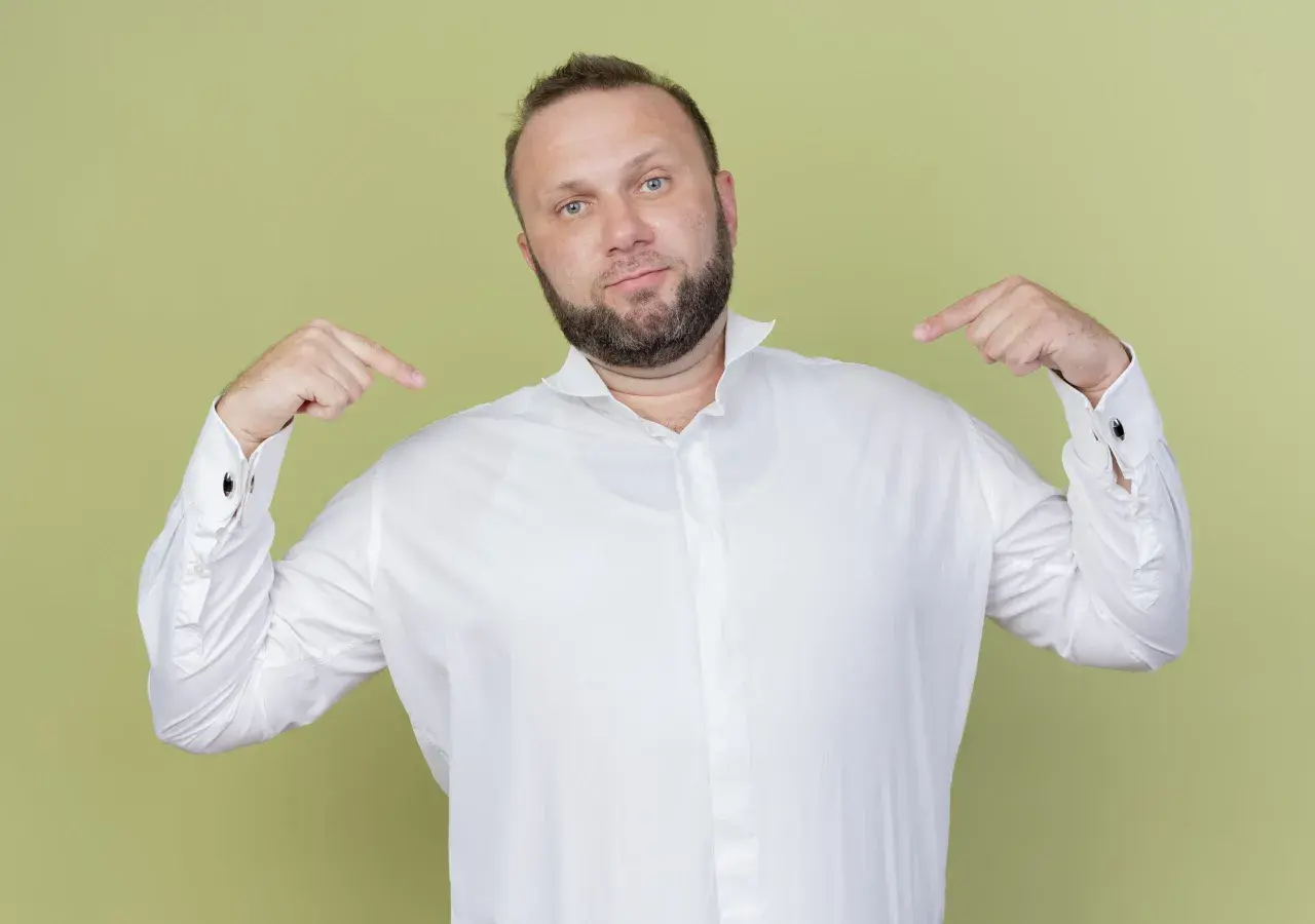Mann zeigt auf sich und sein weißes Hemd. Er fragt sich, welches Unterhemd unter dem Hemd am besten passt.