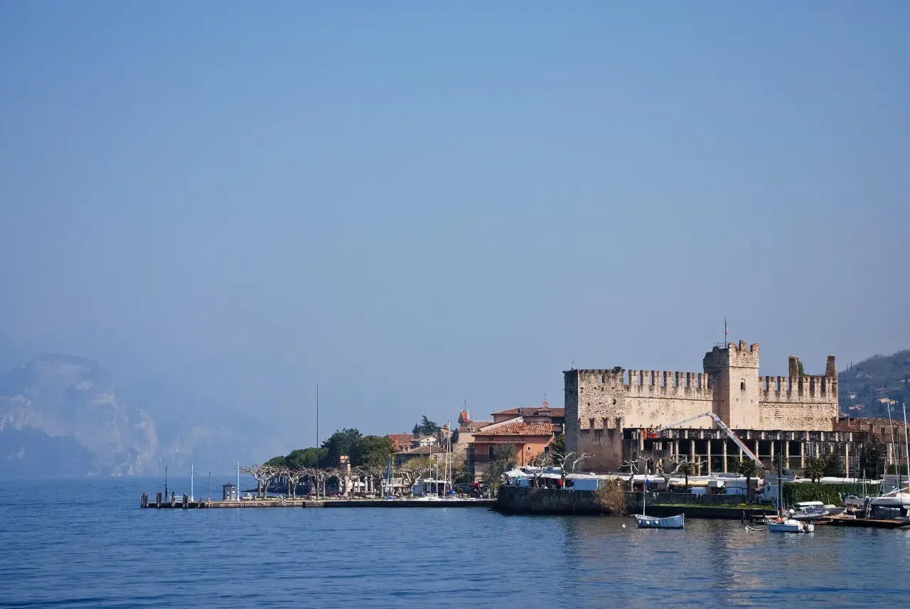 Rocchetta di Moniga del Garda, un gioiello da vedere sul lago. Passeggiata sul lungolago con barche e montagne sullo sfondo.