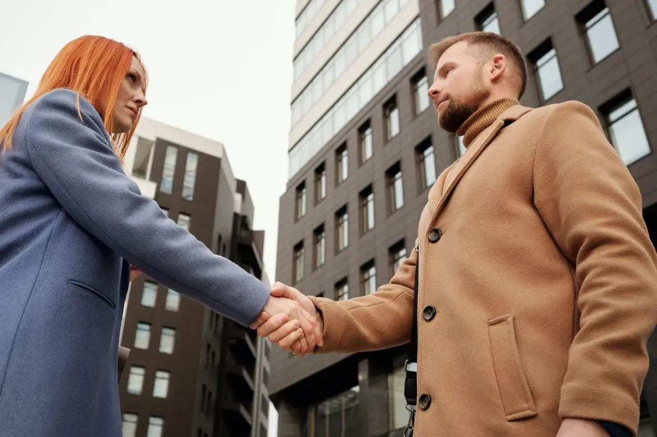 Uomo e donna si stringono la mano davanti a un edificio moderno. Potrebbe essere un incontro tra un paziente e il suo psicologo uomo o donna.