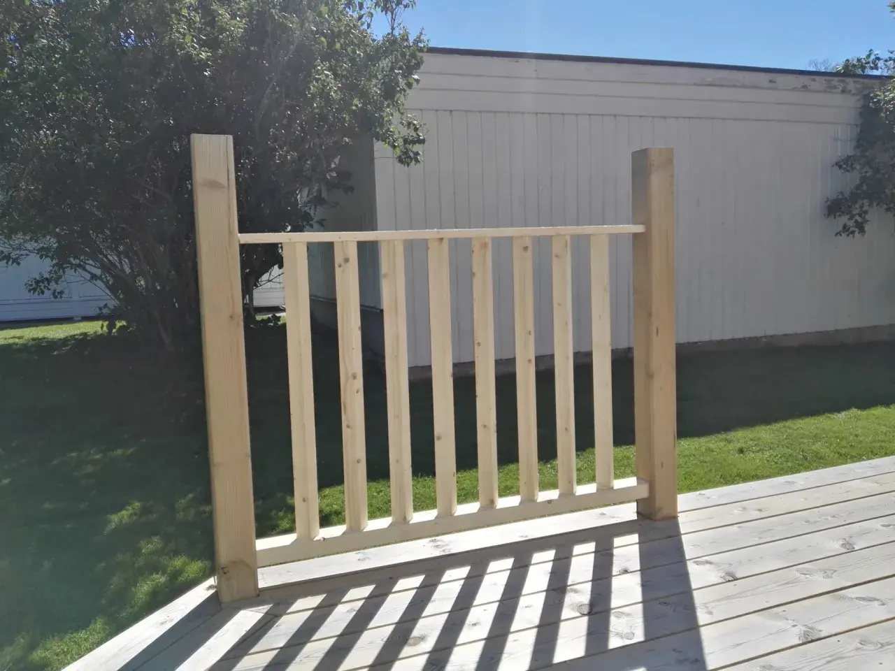 Nybyggt räcke med plank stående ribbor på en altan. Solen kastar skuggor över träet.