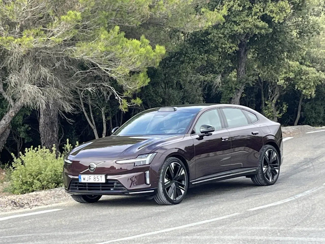 Elegancki, ciemnobrązowy Volvo ES90 na krętej drodze wśród zieleni.