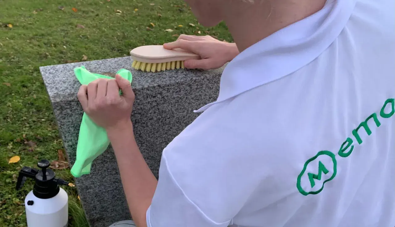 Person cleaning a granite gravestone with a green cloth and a brush.