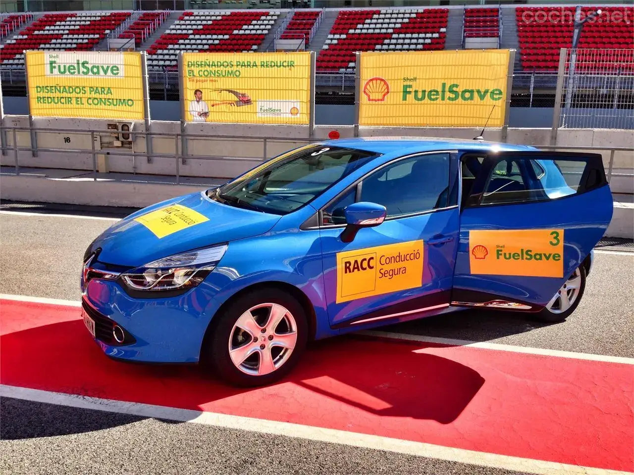 Coche azul en circuito con pegatinas Shell FuelSave, promocionando conducción eficiente.