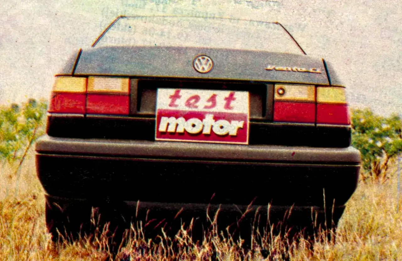 Tylna część Volkswagena Vento z tabliczką "test motor" na tle trawy i krzewów.