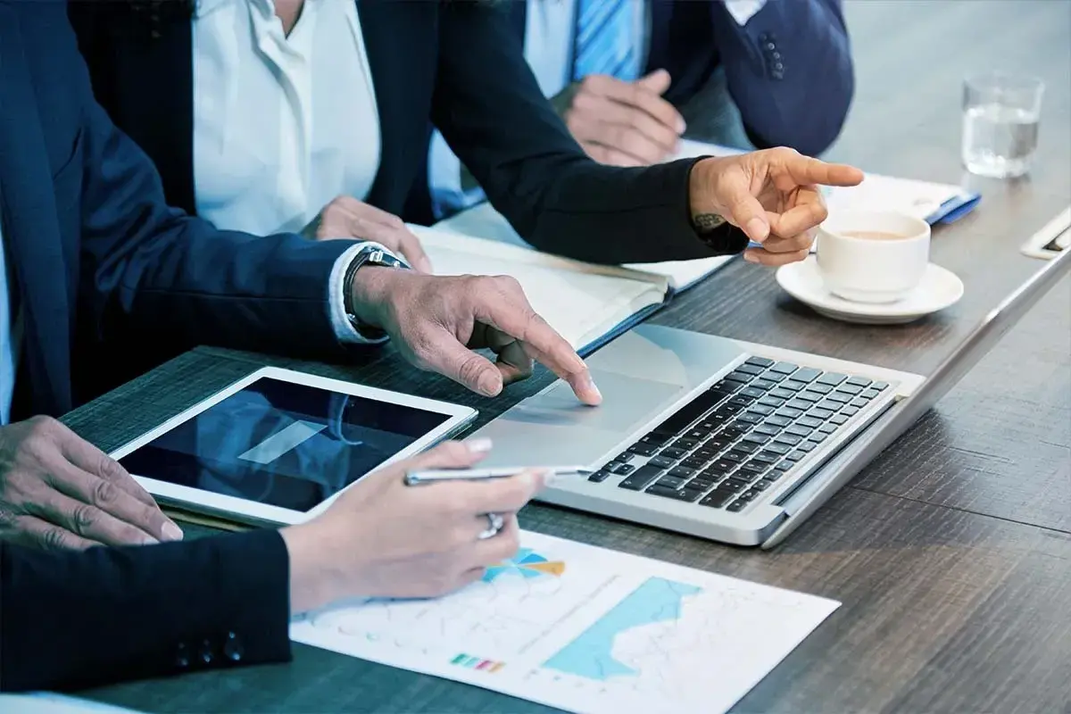 Persone in abiti eleganti collaborano a un tavolo, analizzando dati su tablet e laptop. Sono le risorse umane che lavorano insieme per il successo.