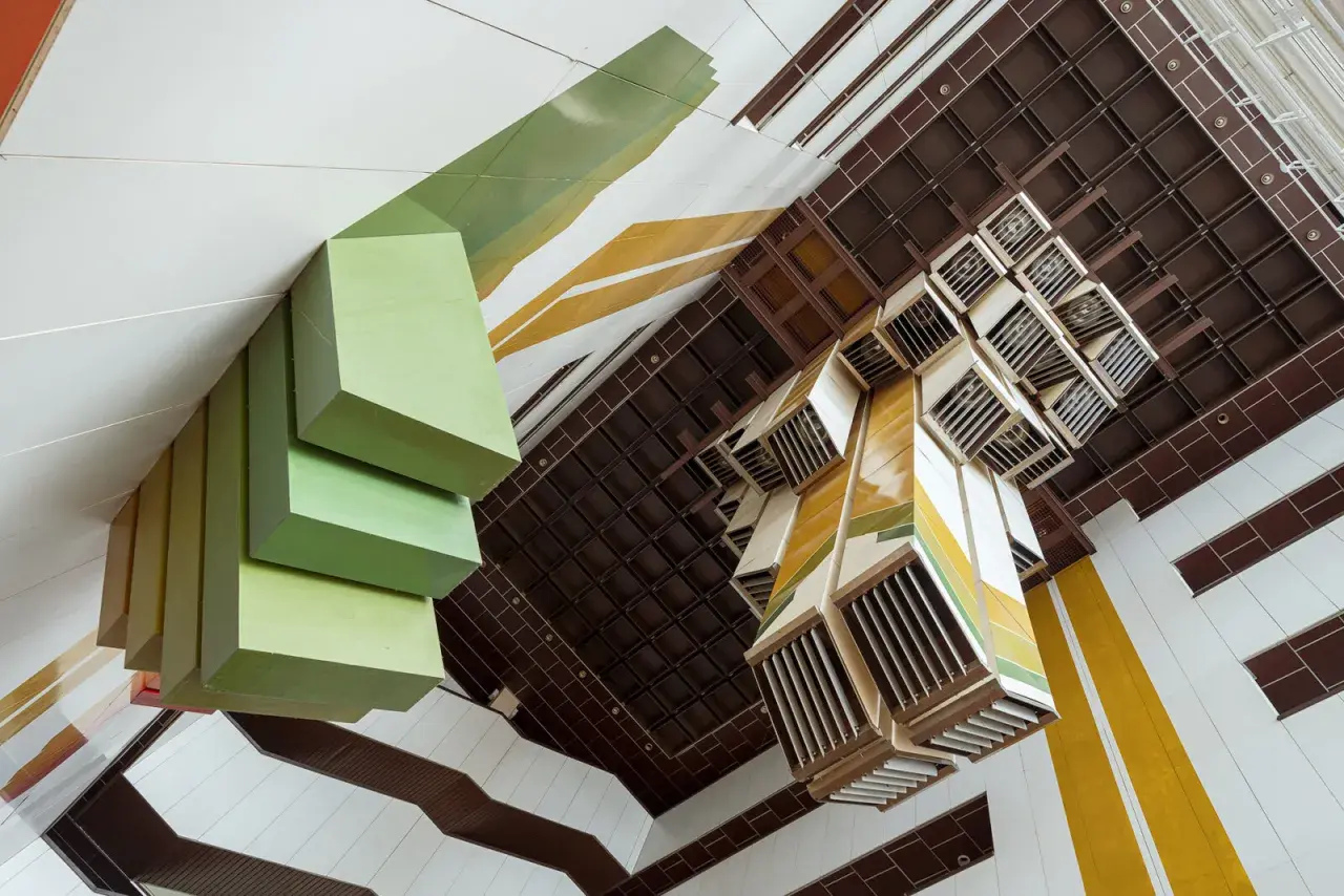Widok z góry na wnętrze budynku z zielonymi, geometrycznymi formami i kasetonowym sufitem. Fotograf architektury uchwycił unikalną perspektywę.