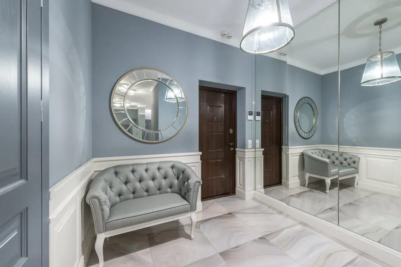 Elegancki, duży reprezentacyjny przedpokój w pałacu z szarą kanapą, ozdobnymi lustrami i dwoma drzwiami.