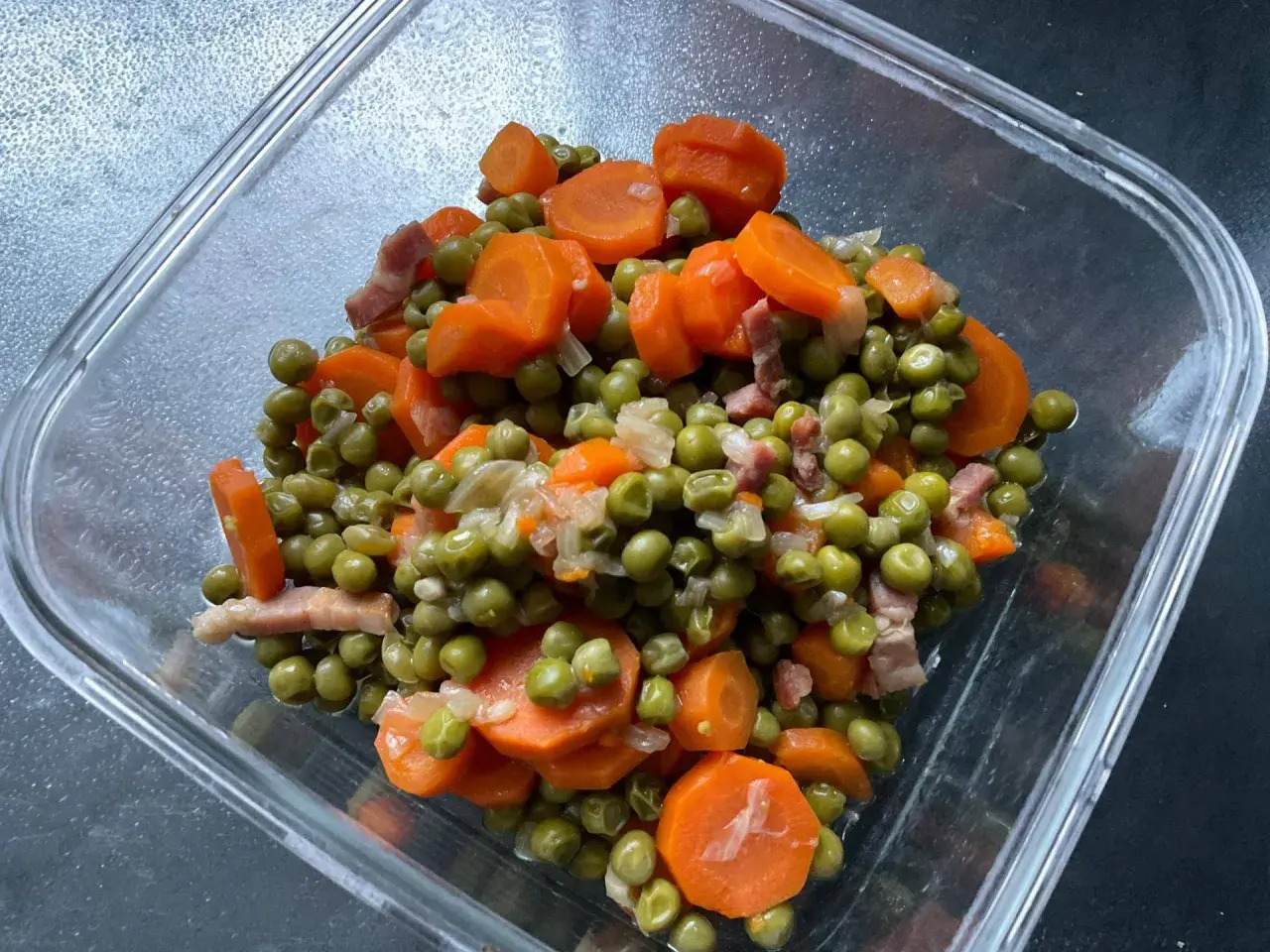 Un plat de petit pois carotte, avec des lardons, dans un récipient en verre. Un classique réconfortant.