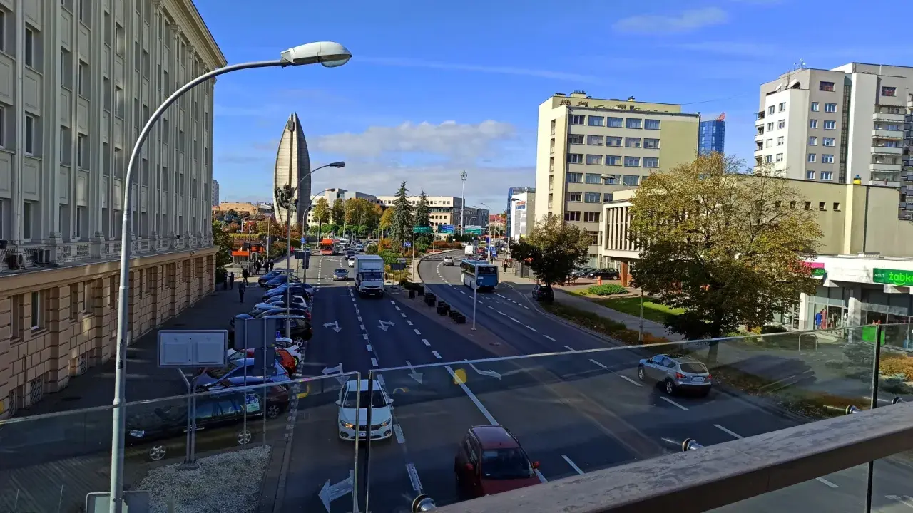 Widok na ruchliwą ulicę w Rzeszowie, z charakterystycznym budynkiem przypominającym żagiel w tle. W oddali widać **ogrody bernardyńskie rzeszów**.