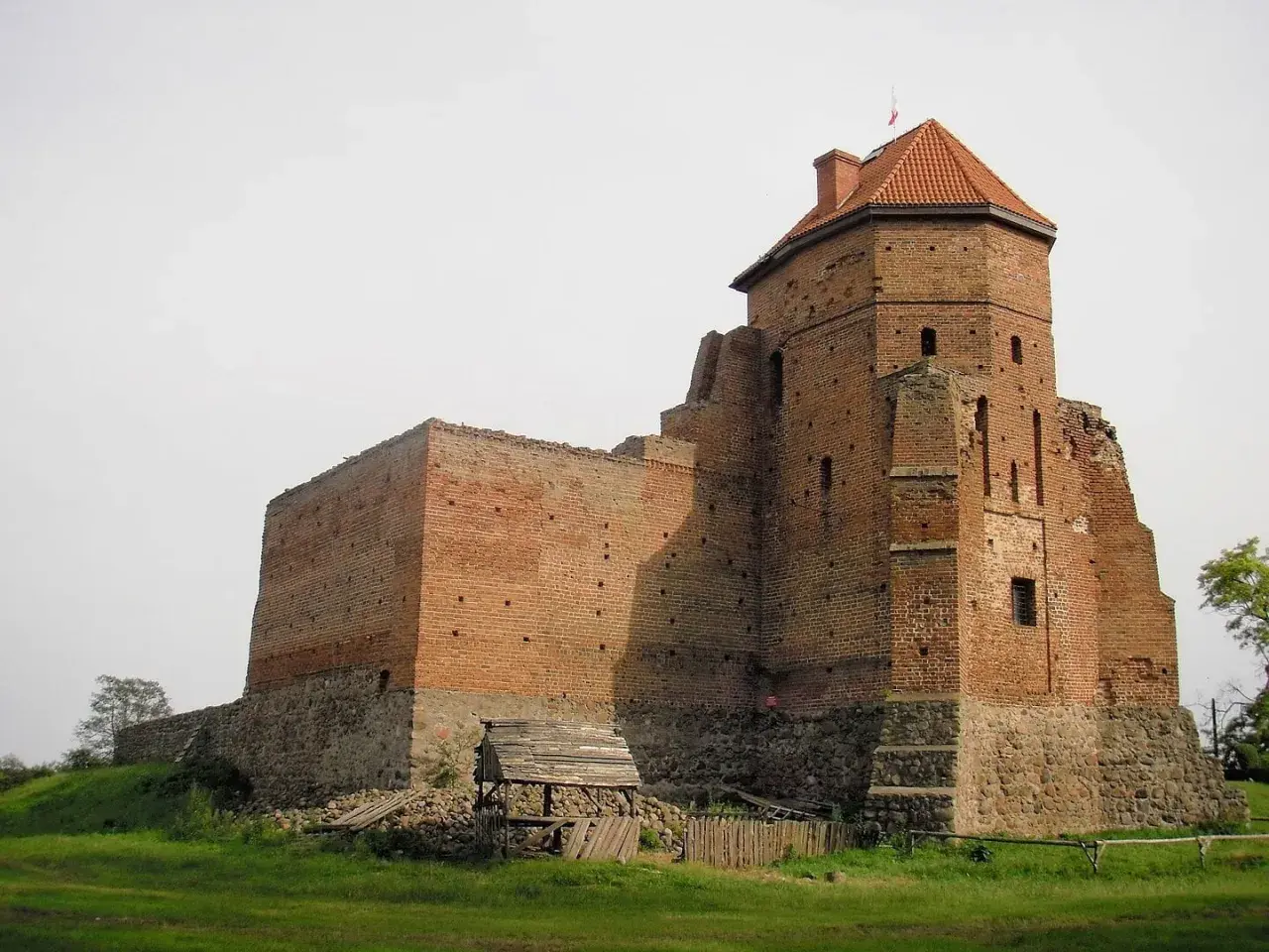 Zamek w Liwie, ceglana twierdza z wieżą i dachem, stoi na wzgórzu.