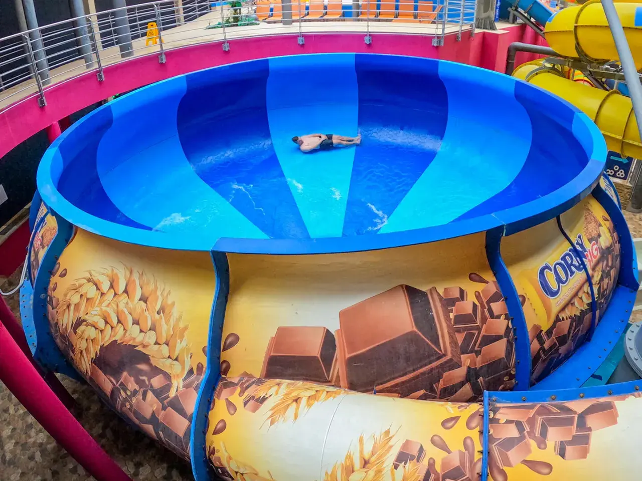 Mann rutscht in einer riesigen blauen Schüssel einer Wasserrutsche, die mit Schokolade und Getreide dekoriert ist. Ein Spaß im Prag!