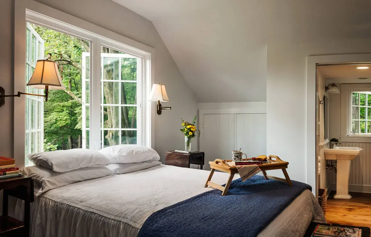 Cozy guest room decor with a bed, breakfast tray, and a window overlooking lush greenery.