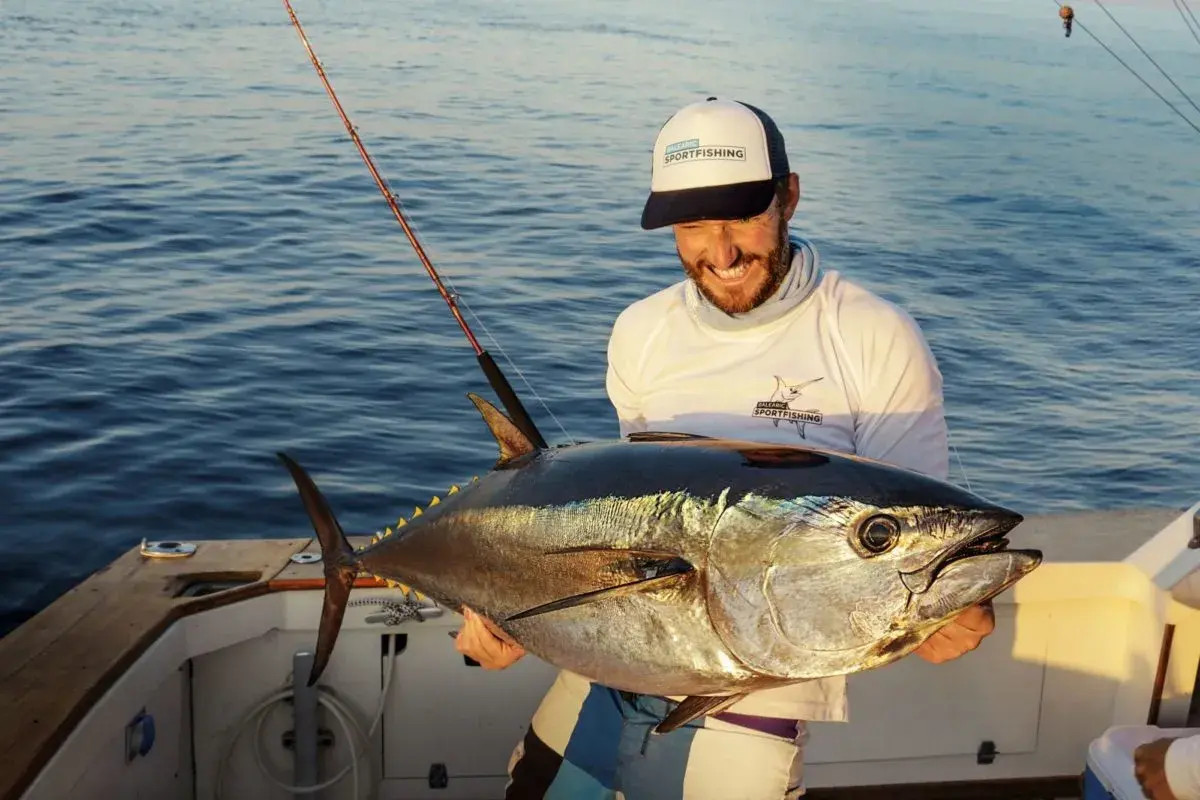Glücklicher Angler hält stolz einen riesigen Thunfisch, den er beim Thunfisch angeln gefangen hat. Das Boot schaukelt sanft auf dem Meer.