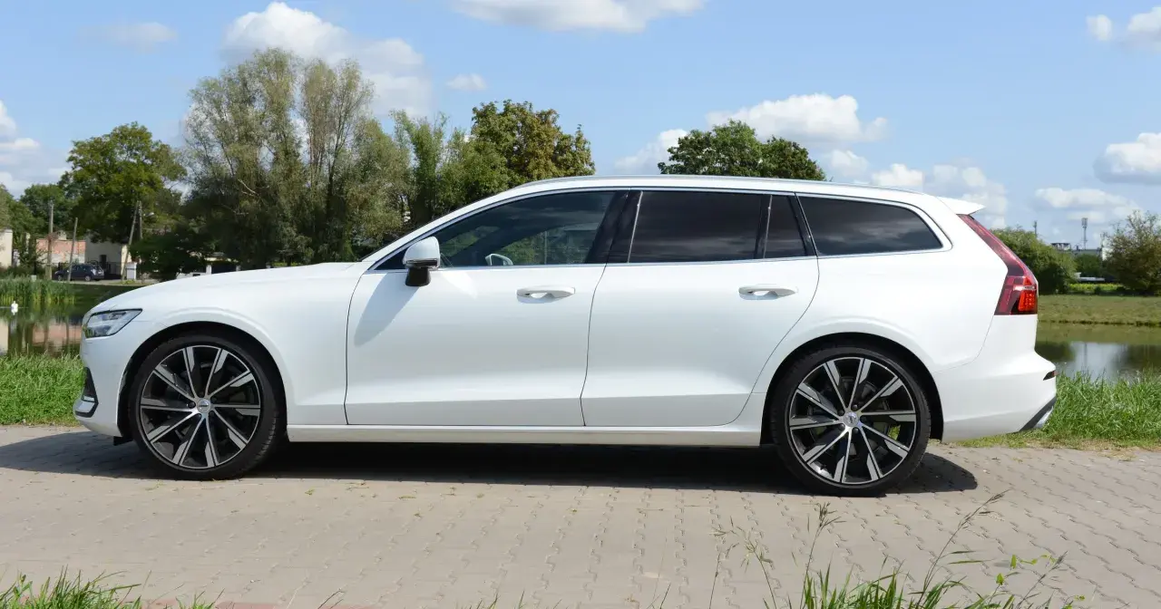 Białe Volvo T6 w wersji kombi stoi na tle zieleni i błękitnego nieba.