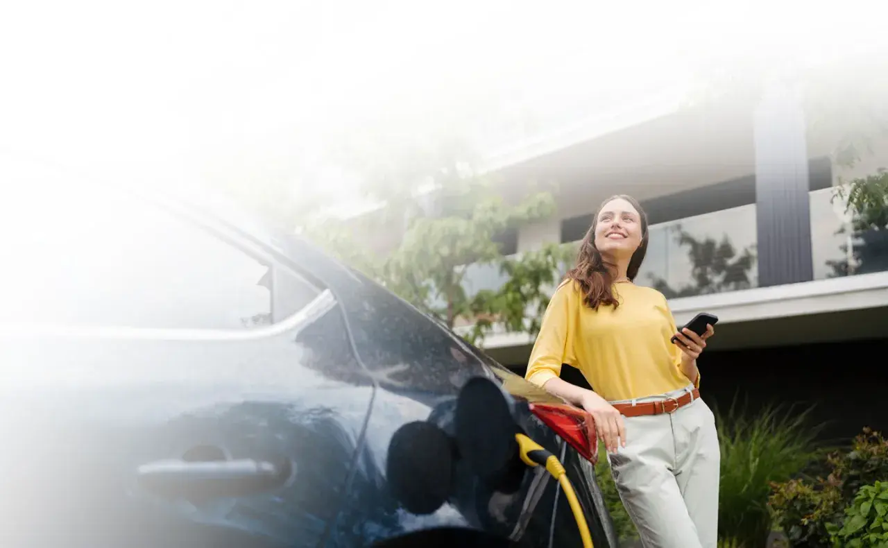 Mujer sonríe mientras carga su coche eléctrico, una elección sostenible que marca la diferencia entre híbrido y eléctrico.