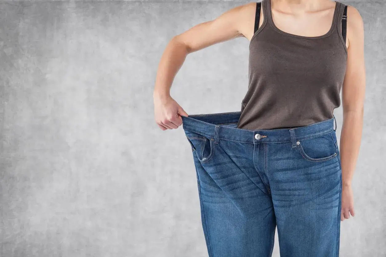 Erfolg beim Gewichtsverlust: Eine Person hält ihre viel zu große Jeans hoch, ein deutliches Zeichen für erreichten Gewichtsverlust.