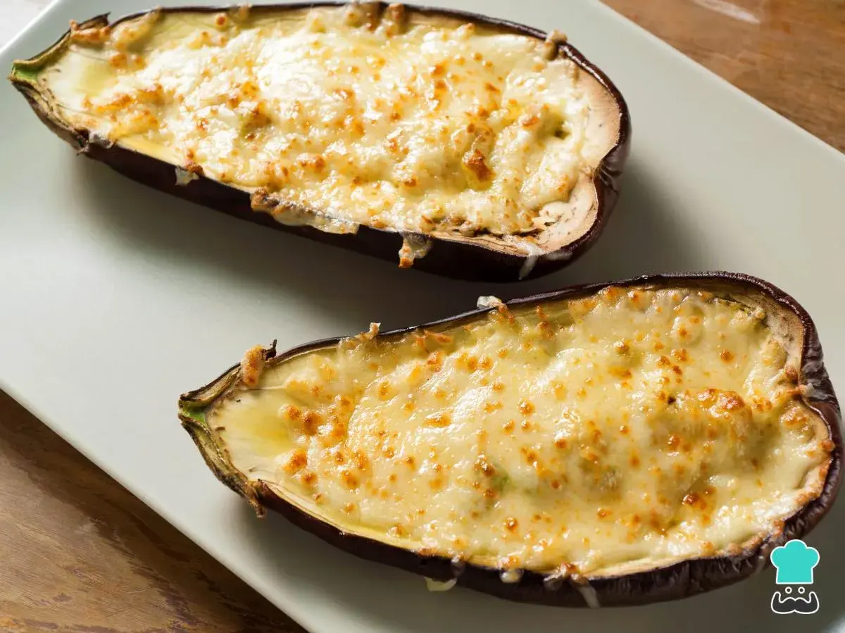 Dos mitades de berenjenas rellenas de carne, gratinadas con queso dorado y burbujeante, listas para disfrutar.