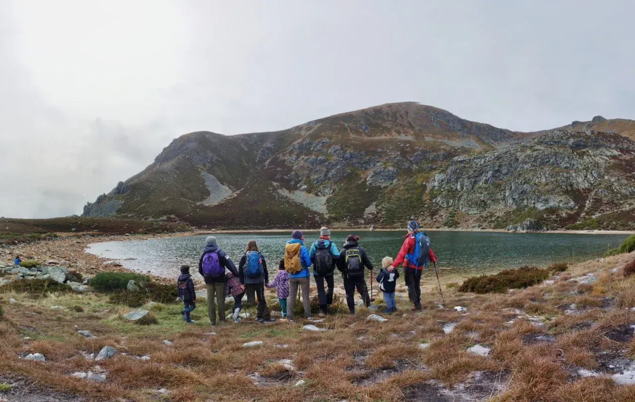 Un grupo de personas, incluyendo niños, disfruta de excursiones en familia junto a un lago rodeado de montañas.