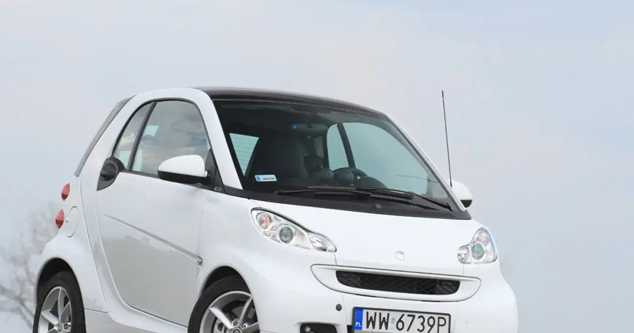 Biały smart fortwo 451 z czarnym dachem, zaparkowany na tle nieba.