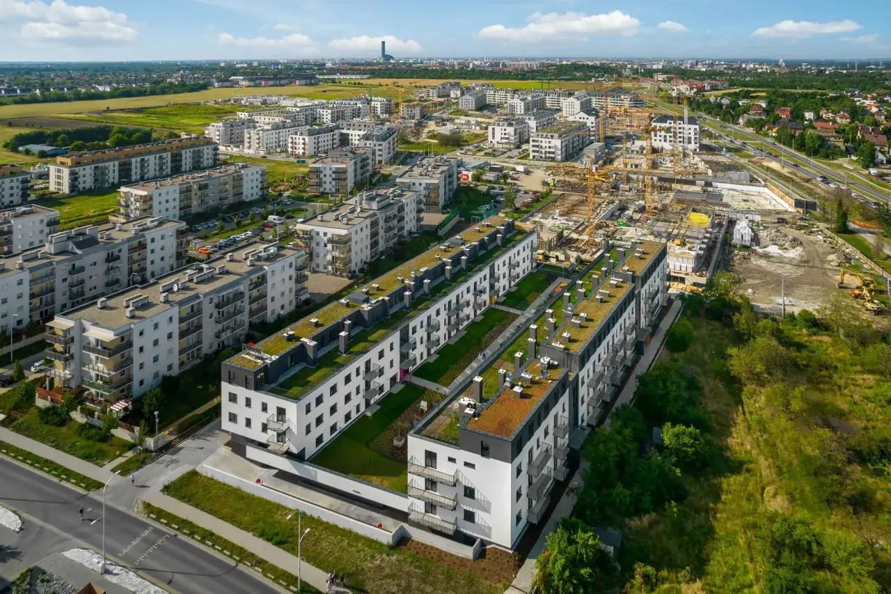 Nowe osiedle z zielonymi dachami, w tle budowa i miasto. Brak śladów powodzi.