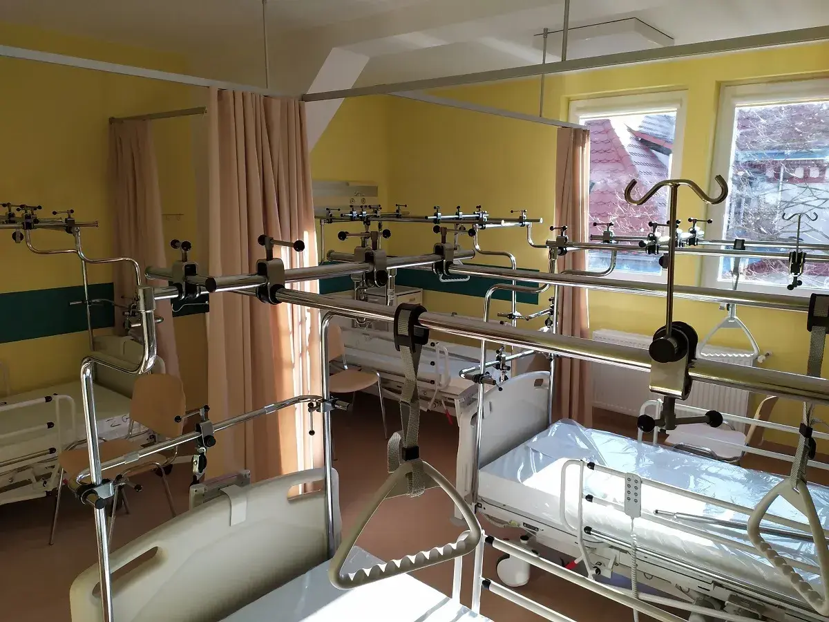 Pokój szpitalny z łóżkami i systemem poręczy nad łóżkami.