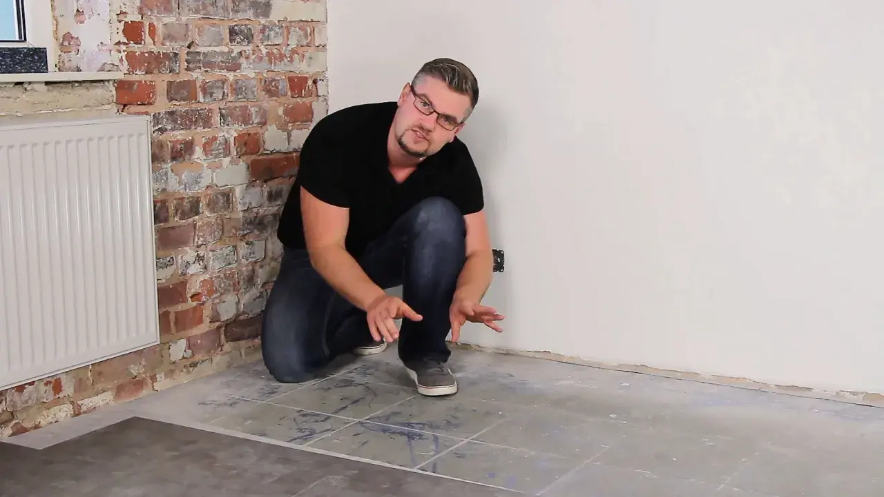 Uomo che mostra la posa pavimento pvc su pavimento esistente, con mattoni a vista e termosifone.