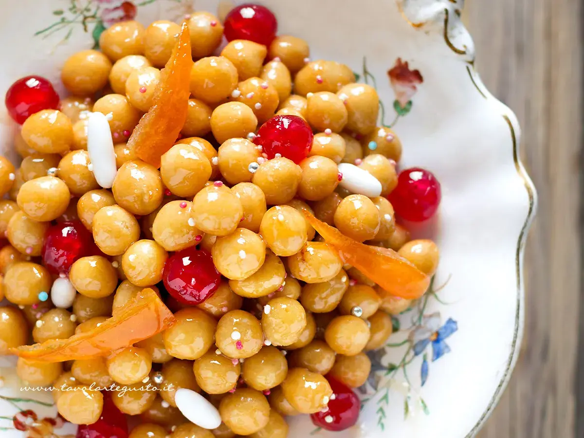 Struffoli ricetta napoletana: palline dorate glassate, decorate con canditi rossi, bianchi e scorzette d'arancia.